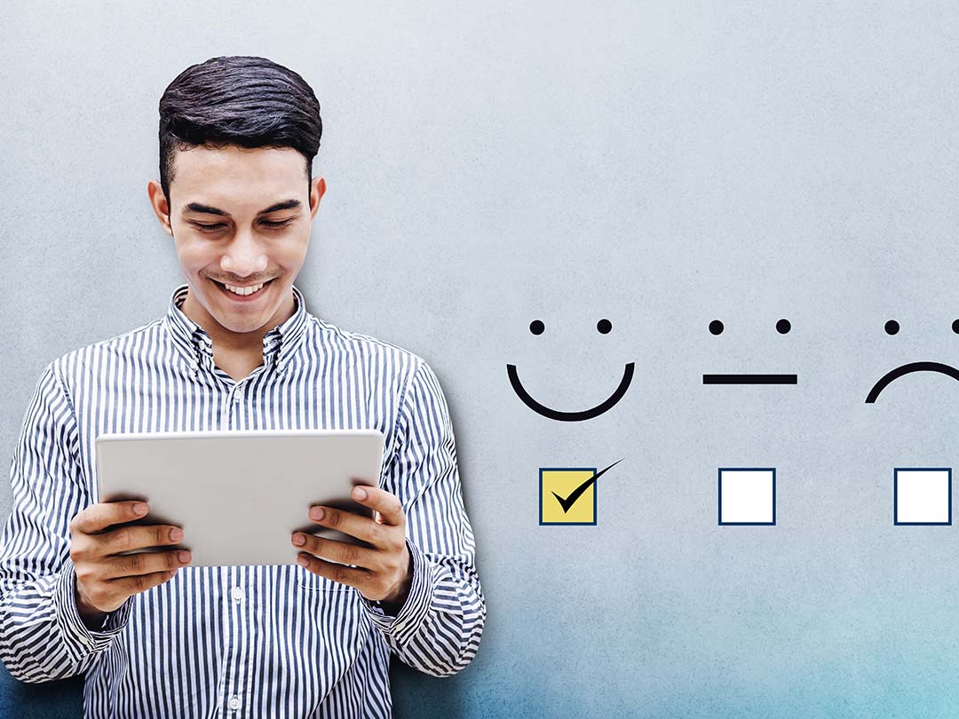 Young man smiling at a tablet in his hands and emojis showing next to him on the background